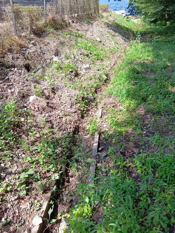 被害の状況1：斜面が掘り起こされて土砂が崩壊し、側溝も埋まっています